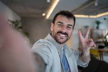 Obraz premium Happy man taking selfie and making victory sign at home