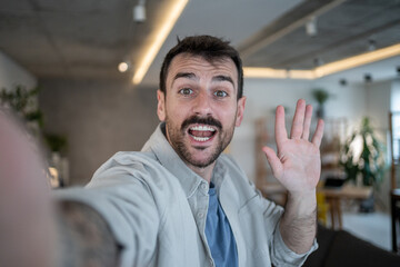 Enthusiastic entrepreneur waving hand during video call in modern office