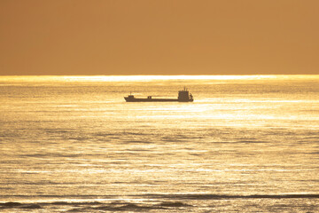 Cargo ship sailing on golden sea at sunset