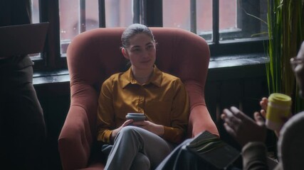 Slowmo shot of young Black male employee chatting with young Caucasian colleagues during coffee break in lounge area of modern office