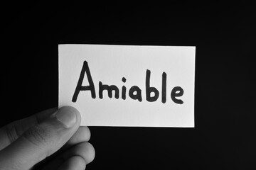 Hand holding a paper card with the word AMIABLE