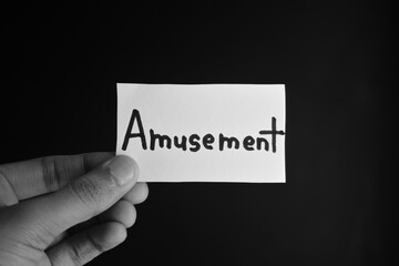 Hand holding a paper card with the word AMUSEMENT