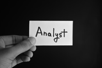 Hand holding a paper card with the word ANALYST