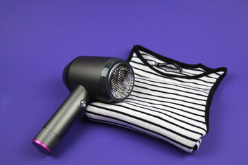 On a purple background lies a T-shirt, and on it is a machine for removing pellets. Concept of clothing care.