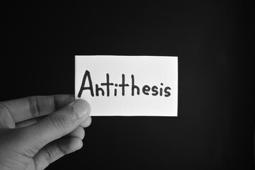 Hand holding a paper card with the word ANTITHESIS