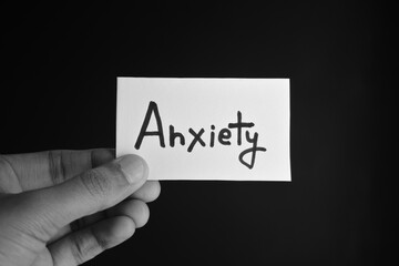 Hand holding a paper card with the word ANXIETY