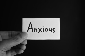 Hand holding a paper card with the word ANXIOUS
