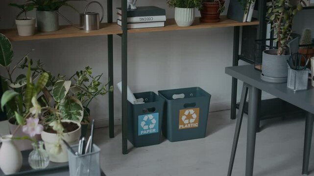 Recycling bins for paper and plastic, indoor plants, and computer with code displayed on monitor in modern eco-friendly office of information technology company