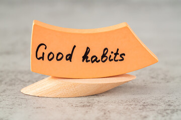 Good habits words on the orange wooden board on the beige stand on gray background. Motivation words for success in life.