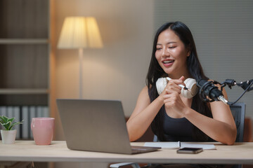 Young asian woman recording engaging podcast content in her home studio, utilizing a professional microphone and laptop while participating in an online interview
