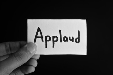 Hand holding a paper card with the word APPLAUD