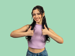 Young woman showing thumbs up with both hands and smiling on green background
