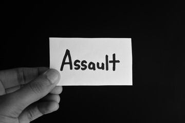 Hand holding a paper card with the word ASSAULT