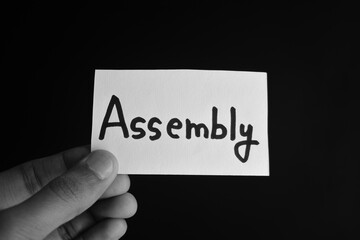 Hand holding a paper card with the word ASSEMBLY