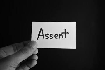 Hand holding a paper card with the word ASSENT