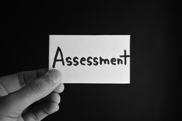 Hand holding a paper card with the word ASSESSMENT