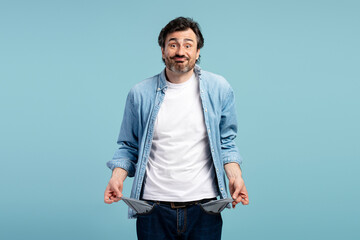Fototapeta premium Pensive man showing empty pockets on blue background