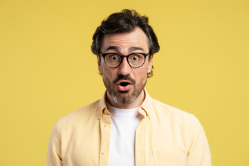 Surprised man opening mouth wearing glasses on yellow background