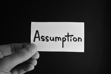 Hand holding a paper card with the word ASSUMPTION