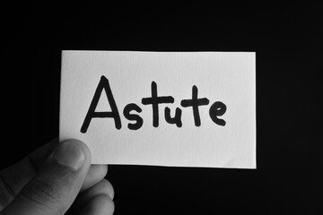 Hand holding a paper card with the word ASTUTE