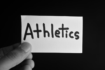 Hand holding a paper card with the word ATHLETICS