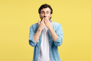 Shocked man covering his mouth with hands on yellow background