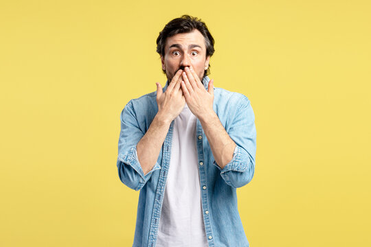 Shocked man covering his mouth with hands on yellow background