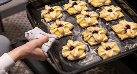 A woman picks baking tray with puff pastry with pineapple wedges wrapped and cherry on top from the oven. Food
