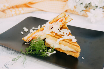 A close-up of a delectable grilled sandwich decorated with shredded cheese and fresh herbs, set against a decorative background, emphasizing a pleasant and inviting culinary presentation.