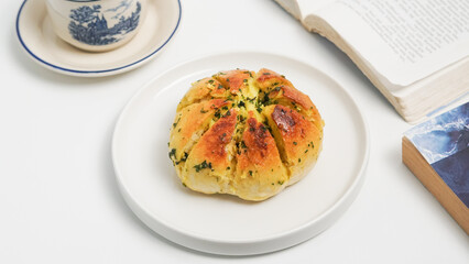 Korean Cream Cheese Garlic Bread with butter sauce and book. Golden-brown, herbed bun with creamy filling on white plate.
