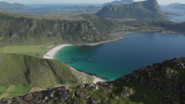 Wide aerial view of ridge and hiking trail of Mannen in Vestv&aring;g&oslash;y, Lofoten, Norway. Going over mountain ridge revealing beaches, bays and turquoise ocean. Drone pushing in, camera tilting down.