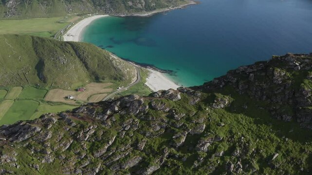 Wide aerial view of ridge and hiking trail of Mannen in Vestv&aring;g&oslash;y, Lofoten, Norway. Going over mountain ridge revealing Haukland Beach and turquoise ocean. Drone pushing in, camera tilting down.