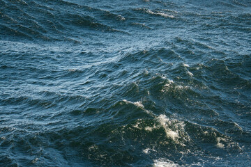 Close-up of dark blue sea water with dynamic waves and foam, natural background or texture.