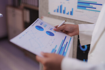 Businesswoman holding and reviewing financial documents with charts and graphs, analyzing data and statistics for business planning and strategy