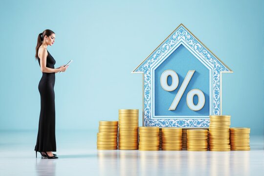 Woman in black dress using tablet near stacked gold coins and ornate house-shaped percentage symbol on light blue background. Business concept.