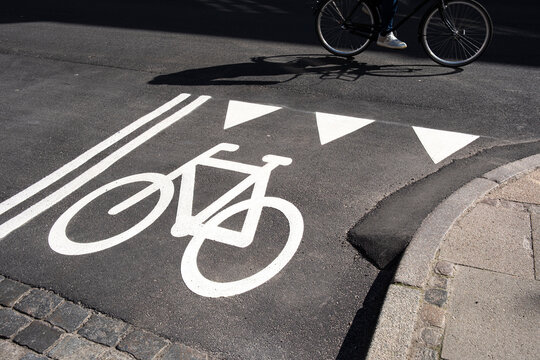 Marked bicycle lane and arrows on asphalt in Copenhagen street corner, clear urban geometry with strong lines and cyclist in motion, transportation concept.