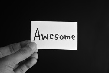 Hand holding a paper card with the word AWESOME
