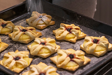 A woman dusts a pineapple wedge and cherry wrapped in a puff pastry with powdered sugar. Baking
