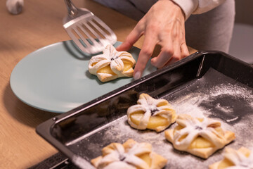 A woman pick the fruit puff pastries with spatula from baking tray and places them on ceramic plate. Baking