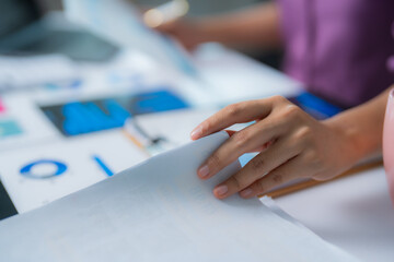 Businesswoman turning page of document while analyzing financial data with charts and graphs, focusing on market trends and investment opportunities