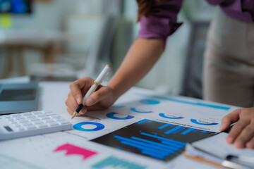 Businesswoman examining financial reports, pointing at pie charts and bar graphs with a pen, using...