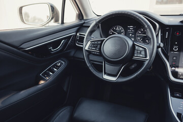 Modern black car interior, leather steering wheel, climate control, large navigation screen, air ducts, deflectors on the car panel. Interior details.