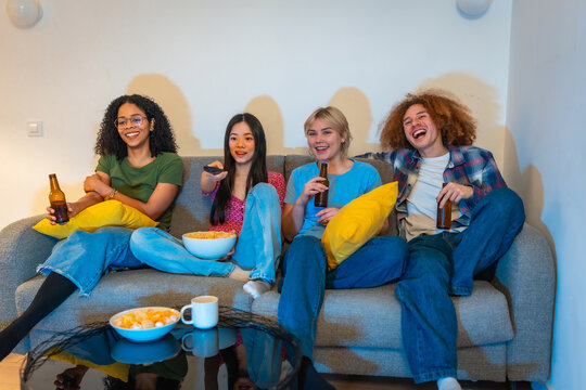Friends watching tv, drinking beer and eating popcorn on sofa - Powered by Adobe