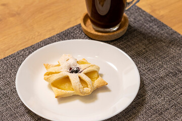 Freshly baked fruit puff pastry on the ceramic plate next to hot cup of coffee. Breakfast