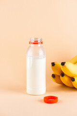 Banana milk in a plastic bottle with bananas on a beige background. Traditional Korean drink. Vertical orientation.