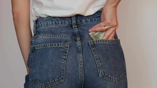 A woman in jeans stows dollars in her pocket in a concentrated manner.
