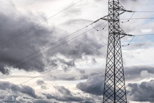 Electricity pylon and power lines under cloudy sky. High voltage infrastructure and energy distribution system in Zaragoza&rsquo;s rural-industrial setting.