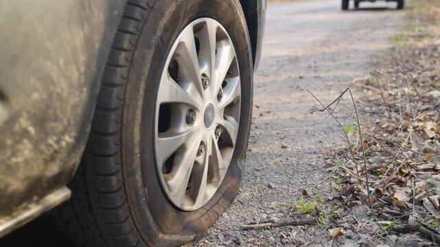 Abandoned vehicle with flat front tire on rough pavement in rural roadside location