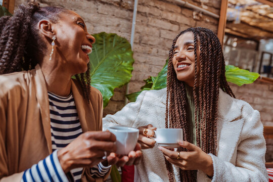 Two cheerful black women sharing a moment of laughter and connection over coffee in a stylish cafe.