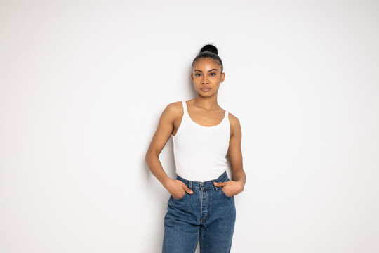 Fashionable woman posing in casual clothing with hands in pockets against a white background